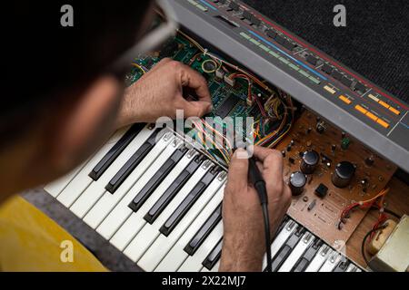 Un technicien en électronique latino-américain répare un piano avec fer à souder et étain au centre de service. Réparation de concept, musique, électronique Banque D'Images