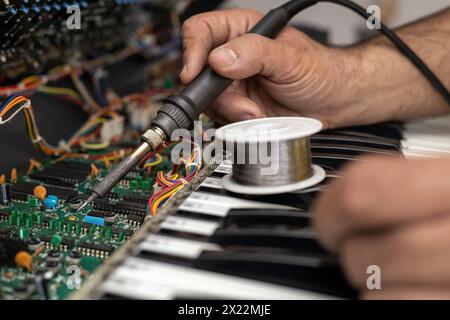 Mains de technicien électronique latino-américain réparant le circuit d'un piano avec fer à souder et étain dans le centre de service. Réparation de concept, Musi Banque D'Images