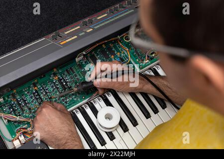 Un technicien en électronique latino-américain répare un piano avec fer à souder et étain au centre de service. Réparation de concept, musique, électronique Banque D'Images