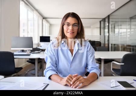 Femme cadre d'âge moyen regardant la caméra assise sur le bureau de travail. Banque D'Images