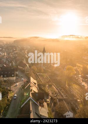 La lumière chaude du matin tombe sur une petite ville avec une tour d'église visible à travers le brouillard, Gechingen, Forêt Noire, Allemagne Banque D'Images