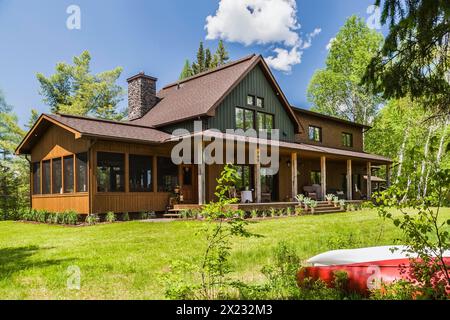 Vue arrière de bois d'épinette teinté brun et vert et bardeau de cèdre maison de campagne certifiée LEED avec véranda à la fin du printemps, Québec, Canada Banque D'Images