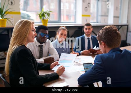 L'équipe multiraciale dans le bureau analyse les graphiques pour le projet. Groupe diversifié comprend patron asiatique, homme d'affaires africain, discutant de stratégie. Multinationale Banque D'Images