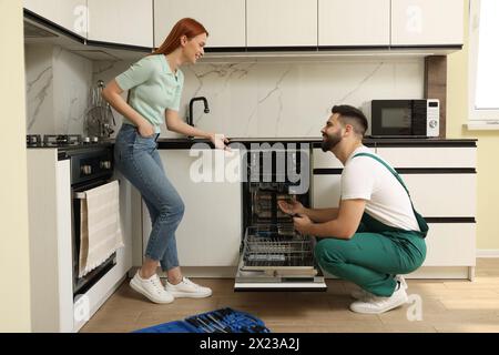 Femme souriante discutant avec réparateur près du lave-vaisselle dans la cuisine Banque D'Images