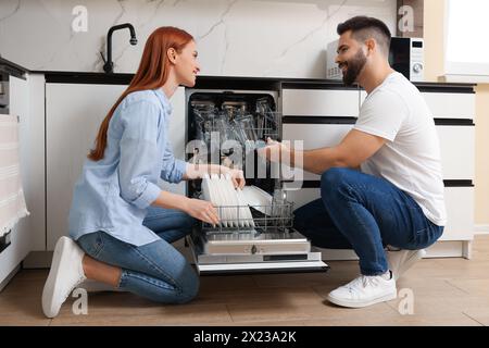 Heureux couple chargement lave-vaisselle avec des assiettes dans la cuisine Banque D'Images