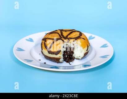 Beignet fourré au chocolat avec morsure retirée, et fourrage au chocolat suintant, sur fond bleu et jolie assiette Banque D'Images