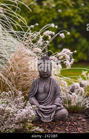 Figure de Bouddha assise en pierre dans le jardin d'herbe exposé dans la neige et la glace Banque D'Images