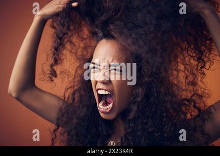 Femme, cheveux bouclés et crier de colère en studio sur fond brun pour les dommages, le traitement et le mauvais résultat. Personne féminine, isolée et bouleversée ou Banque D'Images