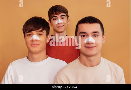 Portrait d'adolescents avec des bandes nettoyantes sur leur nez pour enlever les points noirs. Trois garçons prennent soin de la peau du visage. Procédé cosmétique. Man Banque D'Images