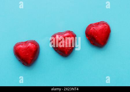 Trois bonbons rouges en forme de cœur reposent en diagonale sur un fond bleu. Banque D'Images