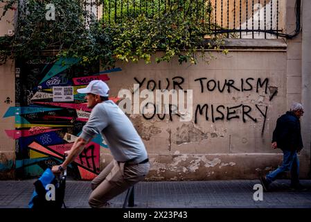 19 avril 2024. Barcelone, Espagne : dans le quartier Gracia de Barcelone, les gens passent devant un graffiti anti-tourisme lisant "votre tourisme, notre misère". Des manifestations contre le tourisme de masse ont lieu depuis des années dans la capitale catalane, l'une des principales destinations touristiques dans le monde. Crédit : Jordi Boixareu/Alamy Life News Banque D'Images
