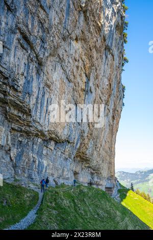 Description : les touristes sur le sentier alpin à la cabane Äscher se tiennent en dessous et regardent l'énorme mur de roche surplombant d'en bas. Seealpsee, Appenzell, Suisse, Banque D'Images