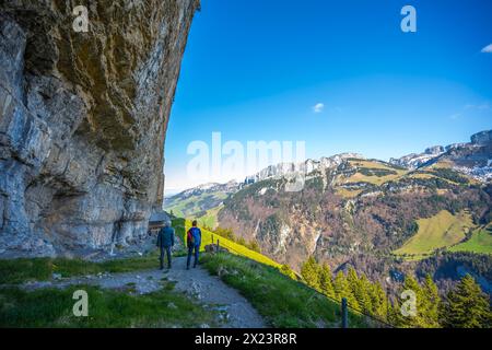 Description : les touristes sur le sentier alpin à la cabane Gasthaus Aescher-Wildkirchli se tiennent en dessous et regardent l'énorme mur de roche en surplomb d'en bas. Seealpsee, AP Banque D'Images