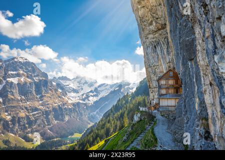 Description : cabane suisse en bois Gasthaus Aescher-Wildkirchli en dessous d'un mur de roche massif et pittoresque chaîne de montagnes en arrière-plan. Seealp Banque D'Images