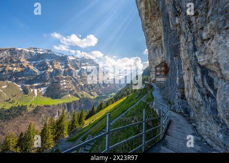 Description : cabane suisse en bois Gasthaus Aescher-Wildkirchli en dessous d'un mur de roche massif surpenchant et d'une chaîne de montagnes panoramique en arrière-plan. Seealpse Banque D'Images