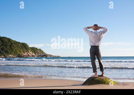 Homme d'affaires debout pieds nus sur un rocher sur la plage et relaxant, Bombinhas, Santa Catarina, Brésil Banque D'Images