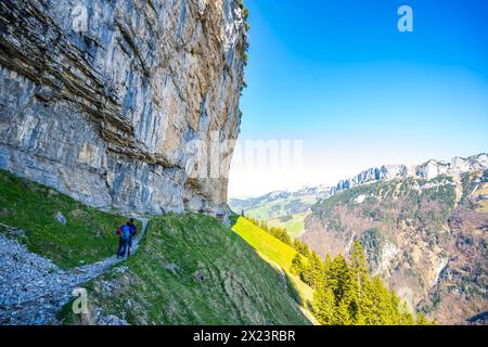 Description : les touristes sur le sentier alpin à la cabane Gasthaus Aescher-Wildkirchli se tiennent en dessous et regardent l'énorme mur de roche surplombant d'en bas. Seealpsee, AP Banque D'Images