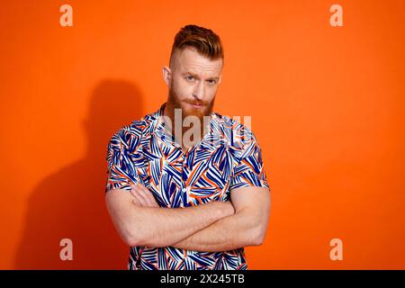 Photo de gars sérieux confiant avec la barbe rouge porter chemise imprimée tenant les bras pliés regardant vous isolé sur fond de couleur orange Banque D'Images