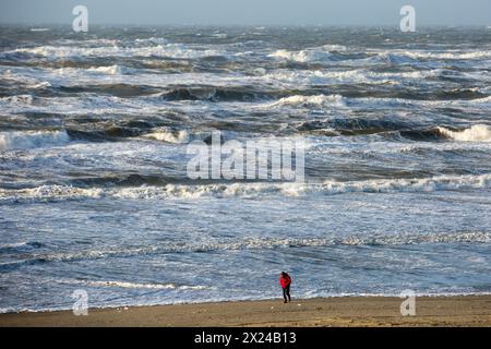 Zandvoort, pays-Bas. 21 décembre 2023. Un homme marche à la plage par temps orageux. Zandvoort est situé sur la mer du Nord aux pays-Bas. La ville est considérée comme l'une des plus grandes stations balnéaires du pays. Ses longues plages de sable et ses dunes côtières attirent des touristes de tous les pays-Bas et de l'étranger pendant les mois chauds d'été. (Photo de Karol Serewis/SOPA images/SIPA USA) crédit : SIPA USA/Alamy Live News Banque D'Images