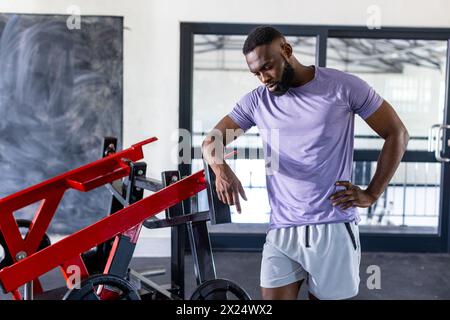 Jeune athlète masculin afro-américain debout à côté de l'équipement de gymnastique dans le gymnase, à l'air réfléchi Banque D'Images