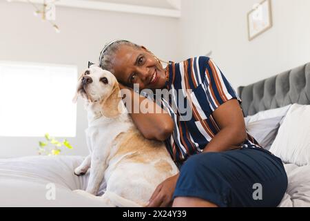 Femme aînée afro-américaine assise avec son chien à la maison, les deux regardant content Banque D'Images