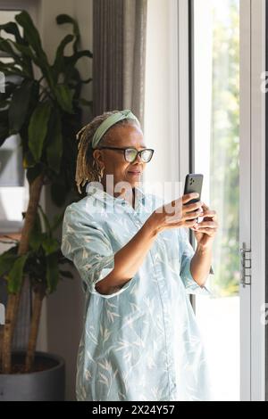 Une femme afro-américaine senior portant des lunettes tenant un smartphone à la maison Banque D'Images