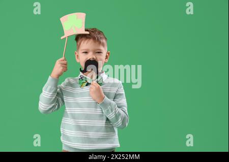 Mignon petit garçon avec chapeau de leprechaun et moustache en papier sur fond vert. Prog Célébration de la fête de Patrick Banque D'Images