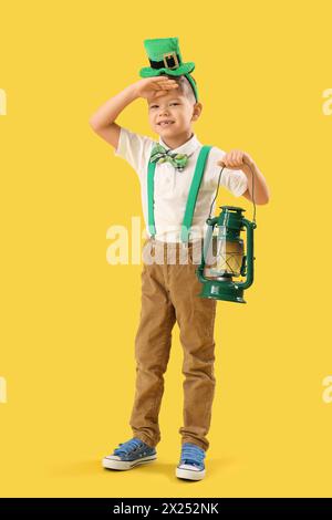 Mignon petit garçon avec chapeau de leprechaun et lanterne sur fond jaune. Prog Célébration de la fête de Patrick Banque D'Images