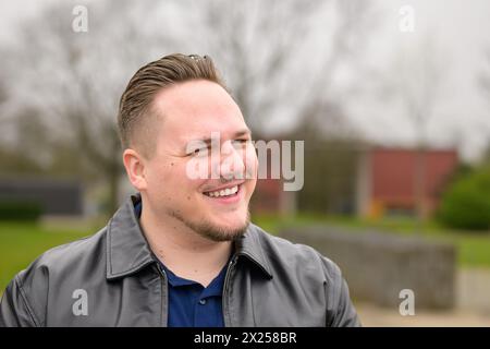 Portrait d'un jeune homme attrayant dans la vingtaine debout à l'extérieur dans un parc au printemps et regardant amical et drôle à la caméra Banque D'Images