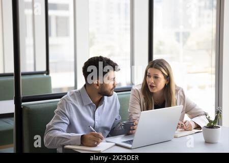 Couple de collègues d'affaires parlant à l'ordinateur portable, assis à la table Banque D'Images