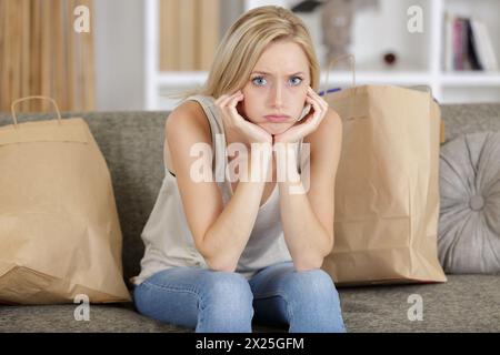 femme grincheuse assise sur le canapé avec des sacs à provisions autour d'elle Banque D'Images