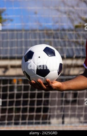 Un jeune athlète afro-américain tient un ballon de football sur un terrain, espace copie Banque D'Images