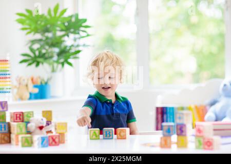 Lettres et chiffres pour l'apprentissage des enfants. Enfant avec des blocs de bois abc colorés. Mots orthographiques de petit garçon avec jouets de bloc éducatifs. Banque D'Images