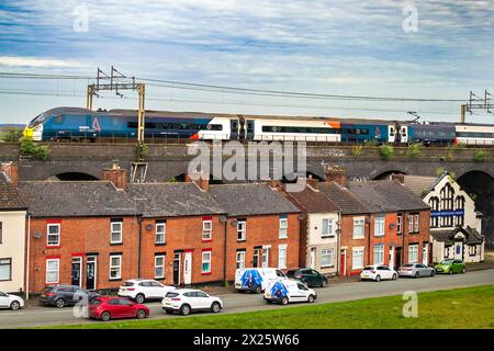 Un train inclinable Avanti Pendolino vu passer au-dessus du viaduc à la gare Runcorn avec des maisons blotties sous le pont. Banque D'Images