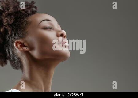 Jeune femme sereine avec les yeux fermés, la tête inclinée vers le haut, exsudant un sentiment de contemplation paisible Banque D'Images