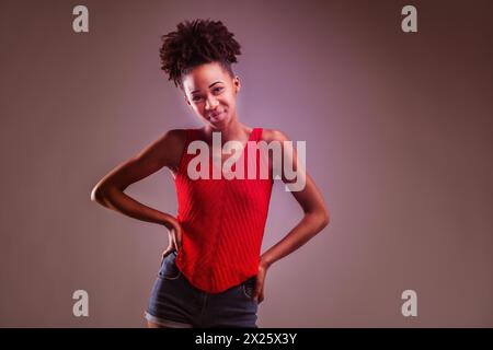 Jeune femme dans un haut en tricot rouge et un short en denim frappe une pose ludique avec un clin d'œil Banque D'Images