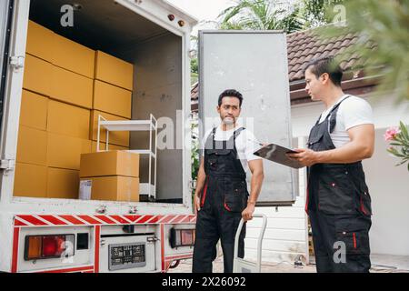 Au milieu du travail d'équipe, les travailleurs du service d'enlèvement effectuent une livraison transparente dans une nouvelle boîte de déchargement à domicile Banque D'Images