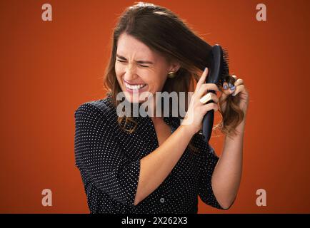 Frustré, femme et brosse pour les cheveux, emmêlé et emmêlé de stress, sec et difficile à peigner. Fond brun, texture et douleur des dommages de Banque D'Images