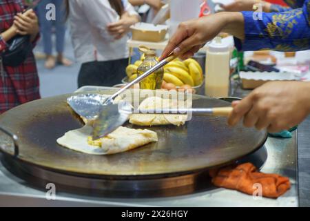 Plongez dans les rues animées de Thaïlande avec cette scène vibrante. Un vendeur qualifié prépare habilement roti croustillant, un plat de Street food apprécié Banque D'Images