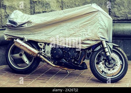 Moto couverte. Moto garée dans une toile de protection, étui. La moto recouverte d'une toile cirée d'une pluie. Parking étanche à l'extérieur du Banque D'Images