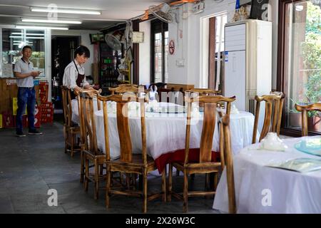 Excursion à Zhujiajiao Water Village, Shanghai, Chine, Asie, restaurant vide avec tables et chaises en bois et un employé visible Banque D'Images