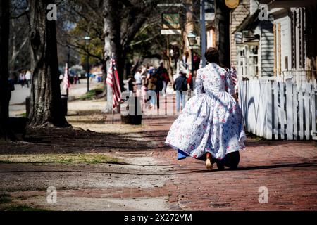 Une femme, en robe d'époque, marche derrière les touristes sur East Duke of Gloucester Street à Colonial Williamsburg. Banque D'Images