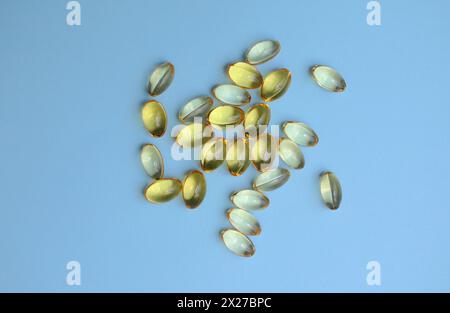 Capsules jaunes d'acides oméga 3 dispersées sur un fond de papier bleu. Banque D'Images