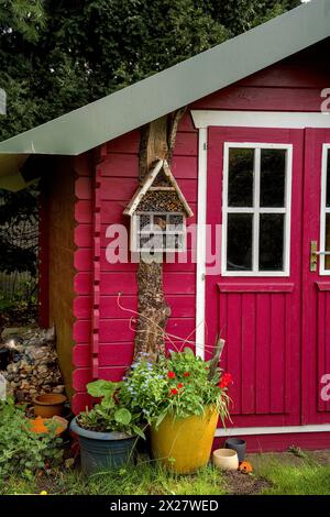 Un petit hangar rouge clair, jardinier, avec quelques outils de jardin autour d'elle Banque D'Images