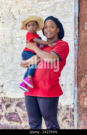 jeune mère du village tenant son bébé, portant un chapeau de paille, debout devant la maison Banque D'Images