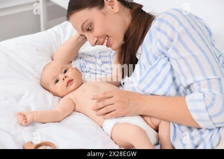 Jeune femme heureuse appliquant la crème pour le corps sur la peau du bébé sur le lit Banque D'Images