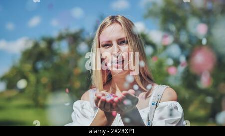 Une fille souffle des confettis en papier multicolores de ses mains. Banque D'Images