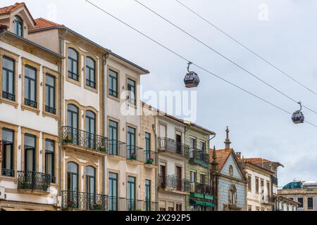 Deux gondoles du téléphérique de Gaia passant juste au-dessus des maisons typiques du quartier de Vila Nova de Gaia, sous un ciel nuageux à Porto. Portugal. Banque D'Images