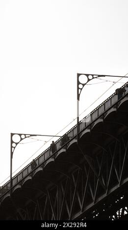 Silhouette de personnes marchant sur la plate-forme supérieure du pont en acier Don Luis I à Porto avec les détails de sa structure métallique et les câbles à travers Banque D'Images