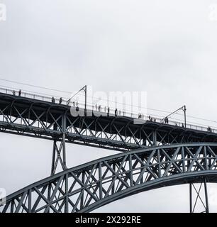 Touristes marchant, prenant des photos et une femme posant depuis la plate-forme supérieure du pont en acier Don Luis I où le métro de Porto passe avec le nuage de pluie Banque D'Images